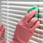 person wearing rubber gloves cleaning window blinds