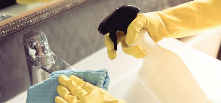 gloved hands of person cleaning bathroom sink
