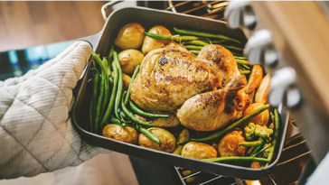 roast chicken and vegetables being taken from oven
