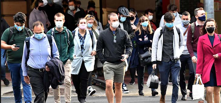 Crowd of people wearing face masks walking across a scramble crossing in Brisbane CBD.