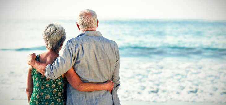 grey haired couple on beach looking at water