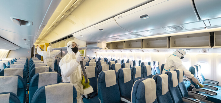 workers in protective gear sanitising empty plane