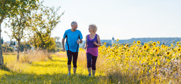 older couple running next to field of yellow flowers