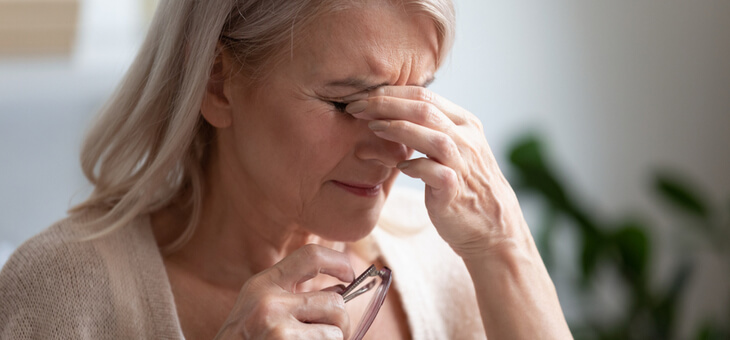 woman holding reading glasses pinching nose between eyes
