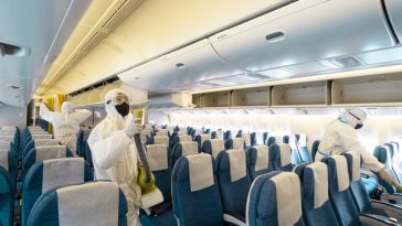 workers in protective gear sanitising empty plane