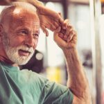 older man in gym stretching arms over head