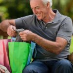 smiling older couple on park bench with shopping bags