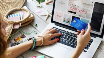 woman holding credit card while shopping at laptop
