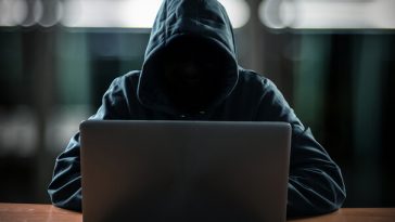 hacker in black hoodie sitting at laptop