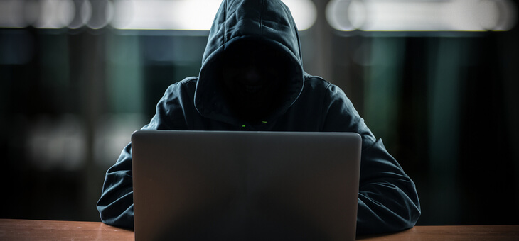 hacker in black hoodie sitting at laptop