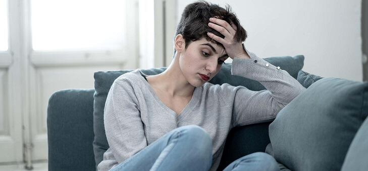 woman sitting on couch with head on hand looking sad