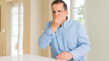 man sitting at kitchen counter holding his nose