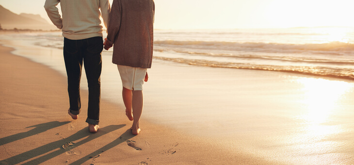 older couple walking on beach at sunset