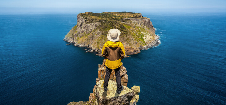 man standing on clifftop looking at distant island