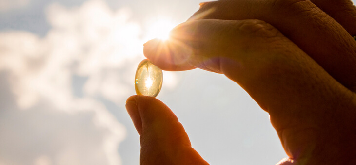 finger and thumb holding translucent capsule up to the sun
