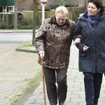 two older women walking arm in arm on footpath