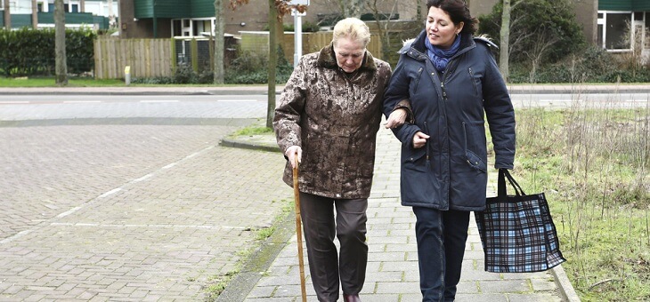 two older women walking arm in arm on footpath