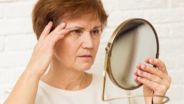 older woman looking concerned at reflection in mirror