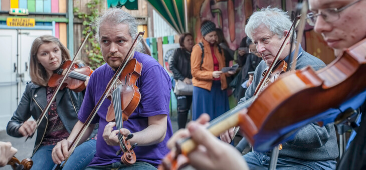 group of three men and one woman playing violins on belfast street