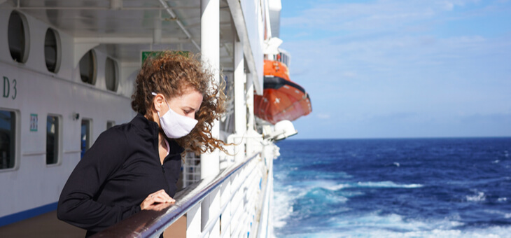 woman leaning over rail of cruise ship wearing surgical mask