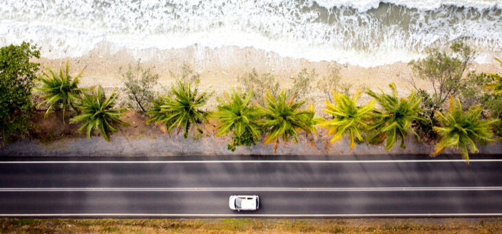 aerial shot of car driving on road running along beach