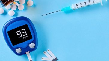 open pill bottle, syringe and blood sugar monitor arranged on blue background