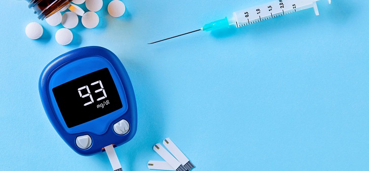 open pill bottle, syringe and blood sugar monitor arranged on blue background