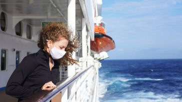 woman leaning over rail of cruise ship wearing surgical mask