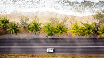 aerial shot of car driving on road running along beach