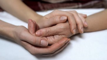 hand of elderly woman held by adult daughter's hand