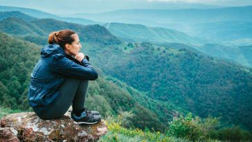 woman sitting on rocky outcrop in forest looking sad