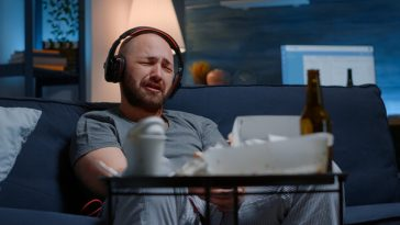 man sitting on couch wearing headphones and crying