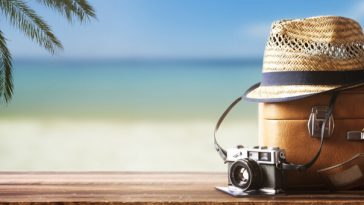 suitcase, hat and camera stacked on beach