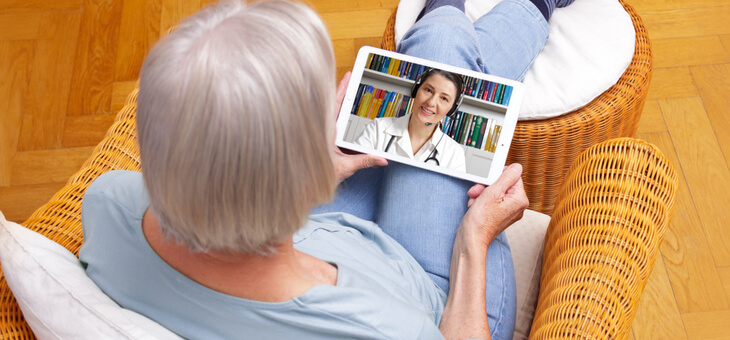 older woman on couch doing telehealth conference with doctor on ipad