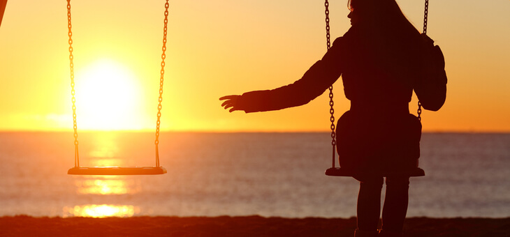 woman on swing at sunset reaching out to empty swing