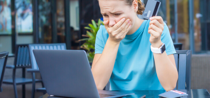 shocked woman holding credit card and looking at laptop