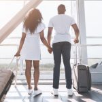 couple holding hands at airport with suitcases