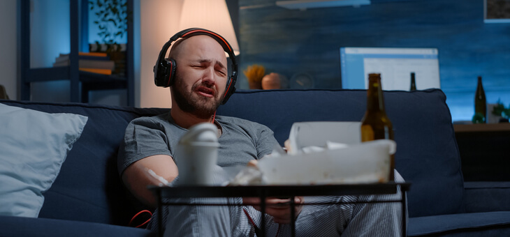 man sitting on couch wearing headphones and crying