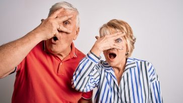 older couple both peeking through hand over face