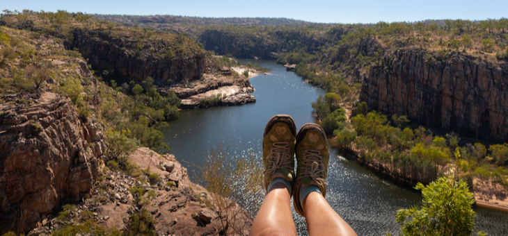 feet wearing hiking boots dangling over cliff above water hole