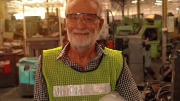 older man in high vis vest working in factory