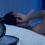 woman lying in bed awake while alarm clock shows 3am