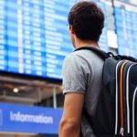 man with backpack standing before airport departure board
