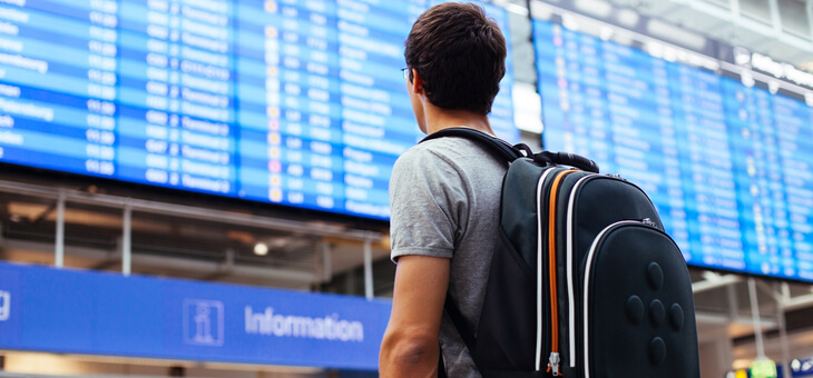 man with backpack standing before airport departure board