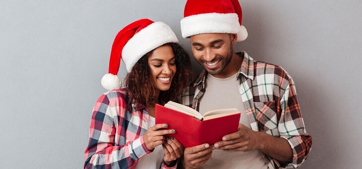couple wearing santa hats sharing a book