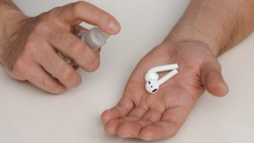 hands holding airpods in one hand and spray bottle in other