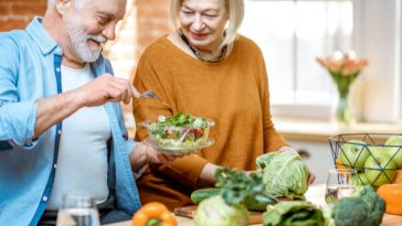 smiling older couple making salad in kitchen