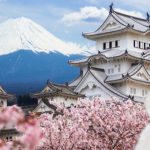ancient japanese temple in front of mountain surrounded by cherry blossom