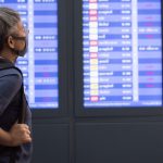 older female traveller wearing face mask looking at departure board
