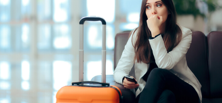 woman sitting at airport gate biting fingernails with suitcase